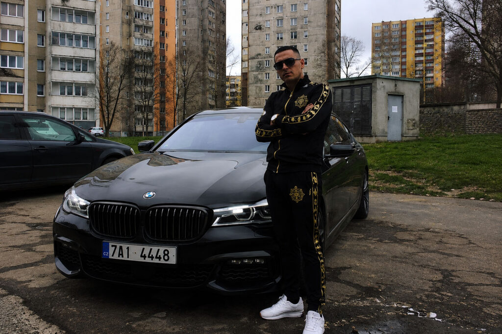 Muž pózující u drahého auta na sídlišti